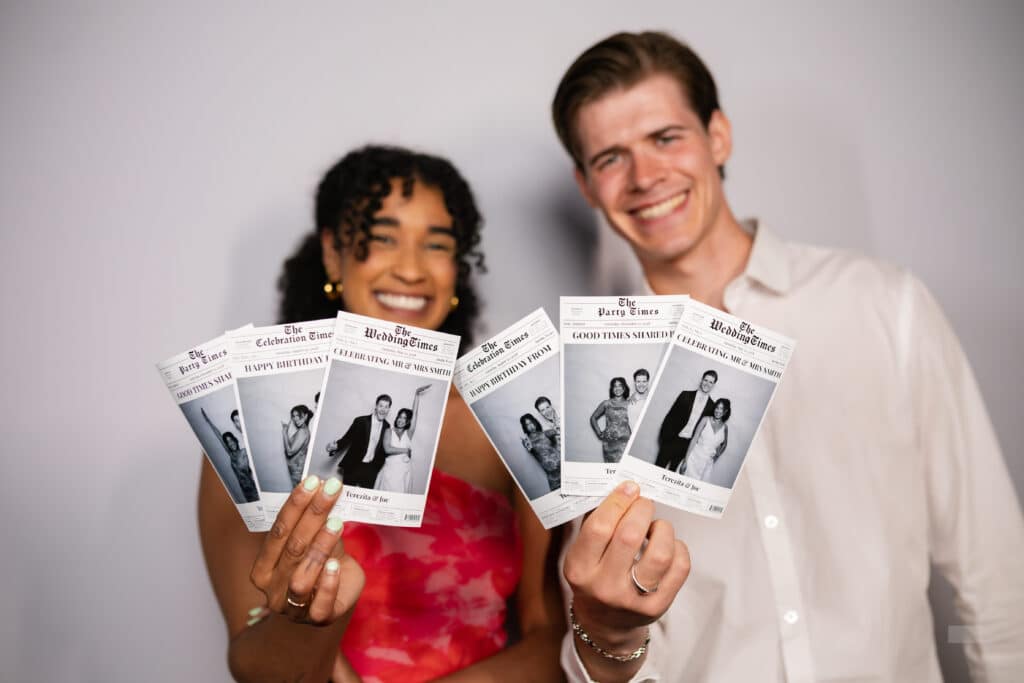 A man and woman holding retro-style news paper photo booth prints